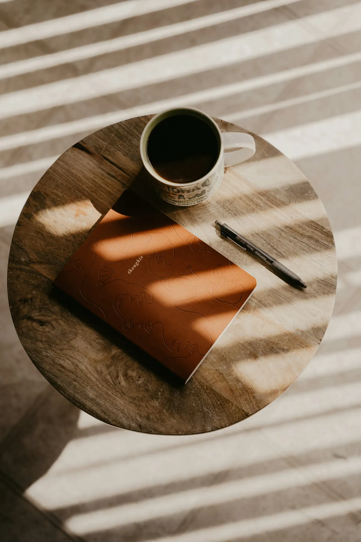 Caderno, caneta e xícara de café sobre a mesa, iluminados pela luz da janela
